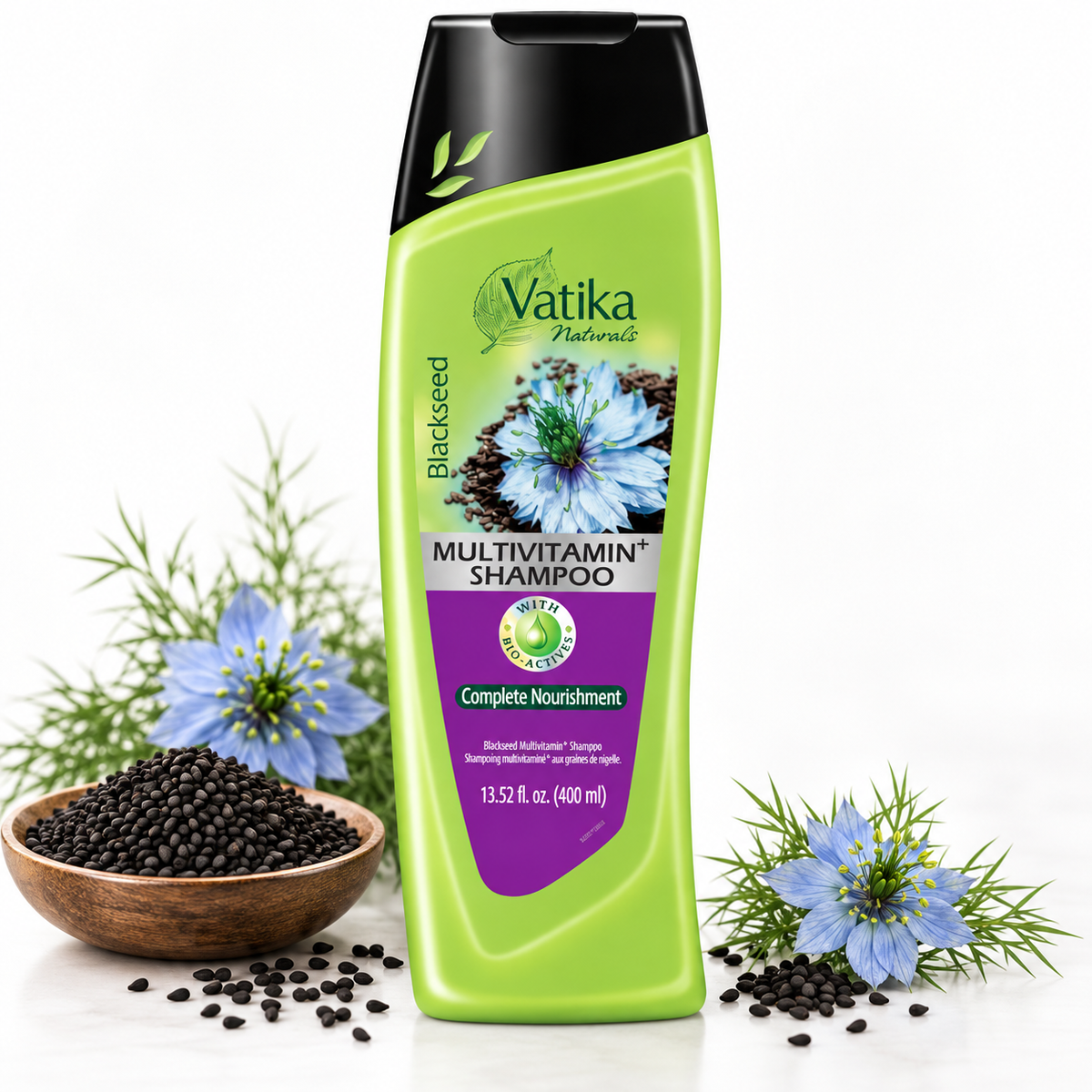A bottle of Vatika Natural Blackseed Multivitamin Shampoo stands on a white surface with decorative black seeds in a wooden bowl, blue flowers, and green leaves around it.